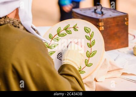 Young woman seamstress sewing a simple drawing, disguised as medieval in a traditional craft children's exhibition. Stock Photo