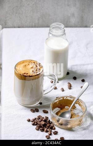 Dalgona frothy coffee trend korean drink milk latte with coffee foam in glass mug, decorated by ground coffee on white cotton table cloth. Ingredients Stock Photo
