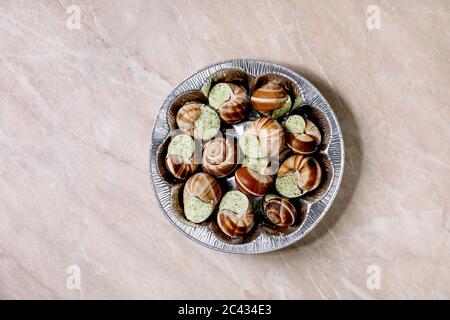 Frozen Uncooked Escargots de Bourgogne - Snails with herbs butter, gourmet dish, in store aluminum packaging over pink marble background. Flat lay, sp Stock Photo