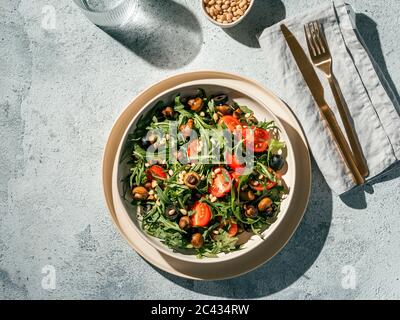 Salad with arugula, mini champignons, cherry tomatoes, black olives, pine nuts. Top view or flat lay. Copy space. Hard light. Horizontal Stock Photo