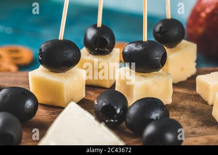 Cheese cubes and black olives on a wooden board with crackers on the blue table Stock Photo