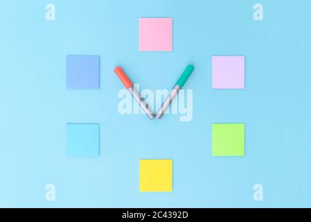 Clock made of colorful stickers and markers on blue background. Copy space, flat lay. Concept office and back to school. Stock Photo