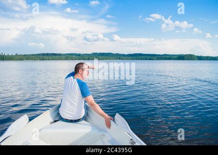 Man sitting on his back to the boat and looking at the beautiful landscape of the lake in the depths of Finland. Concept vacation on the lake. Stock Photo