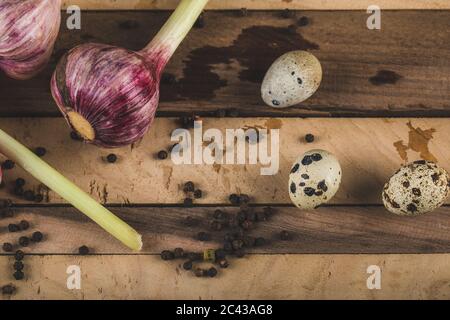 Quail eggs in a small pot with pink garlics and pepper balls on a wooden board Stock Photo