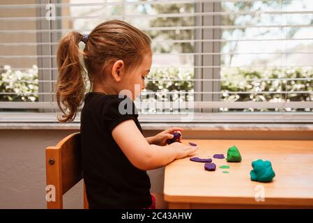 Close up of child playing with play dough in a playroom on a wood table. Girl molding modeling clay. Child playing and creating from play dough. Stock Photo