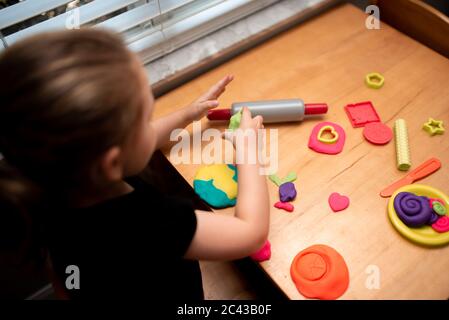 Close up of child playing with play dough in a playroom on a wood table. Girl molding modeling clay. Child playing and creating from play dough. Stock Photo