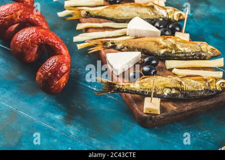 Snack board with sausage slices, cheese cubes and black olives with crackers and dry fish on the blue table Stock Photo