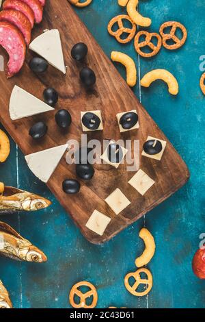 Sausage slices with cheese cubes, olives and crackers with dry fish on the blue table, top view Stock Photo