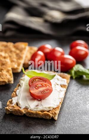 Dieting knackebrot. Crispbread with creamy cheese, cherry tomato and basil leaf on kitchen table. Stock Photo