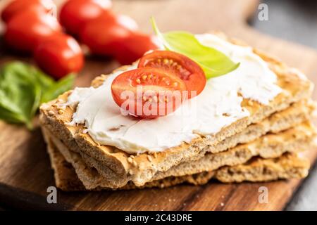 Dieting knackebrot. Crispbread with creamy cheese, cherry tomato and basil leaf on kitchen table. Stock Photo