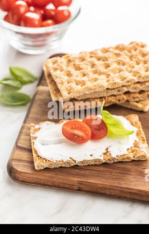 Dieting knackebrot. Crispbread with creamy cheese, cherry tomato and basil leaf on kitchen table. Stock Photo