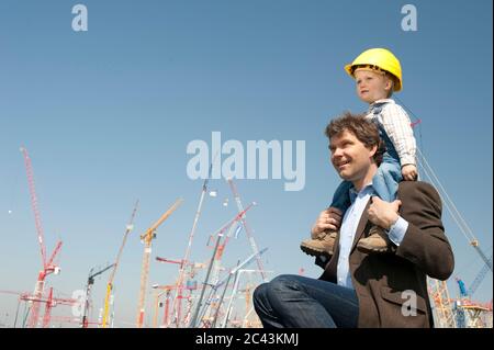 Father and son with hard hat in front of construction cranes Stock Photo