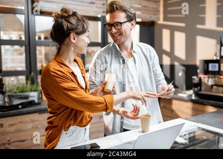Two young managers or shop owners having some discussion at the counter of the shop or cafe. Small business management concept Stock Photo