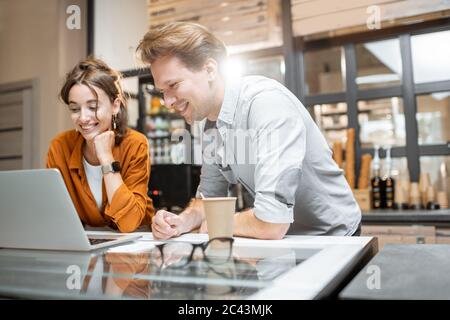 Two young managers or shop owners having some discussion working on a laptop at the counter of the shop or cafe. Small business management concept Stock Photo