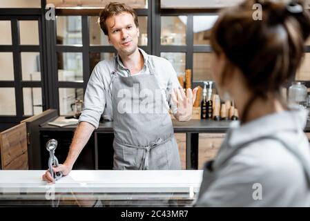 Portrait of a cheerful salesman in apron talking with a customer at the small shop or cafe. Concept of a small business and work in the field of services Stock Photo