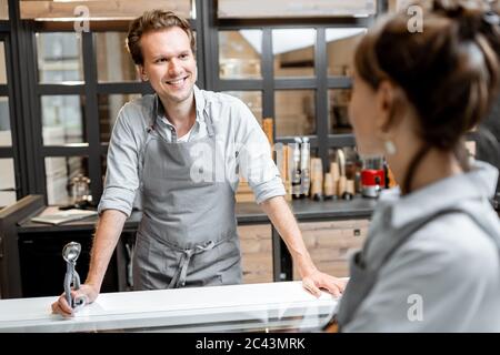 Portrait of a cheerful salesman in apron talking with a customer at the small shop or cafe. Concept of a small business and work in the field of services Stock Photo