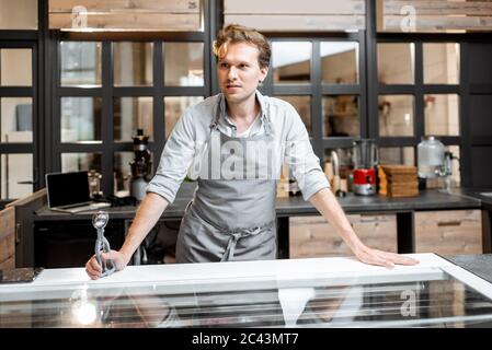 Portrait of a cheerful salesman in apron standing behind the counter of a small shop or cafe. Concept of a small business and work in the field of services Stock Photo