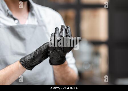 Seller in black gloves disinfecting hands while working in a grocery store or cafe, close-up view. Concept of a new rules for business during a pandemic Stock Photo