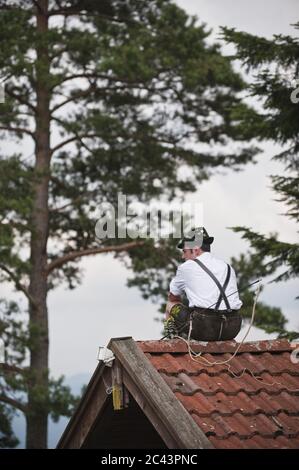 Man with a whip to click Goaßlschnalzen sits on the roof Stock Photo