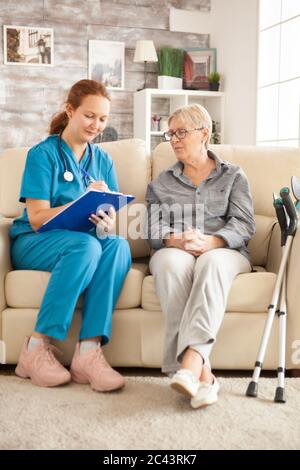 Young female doctor taking notes on clipboard while having a conversation with senior woman in nursing home. Stock Photo
