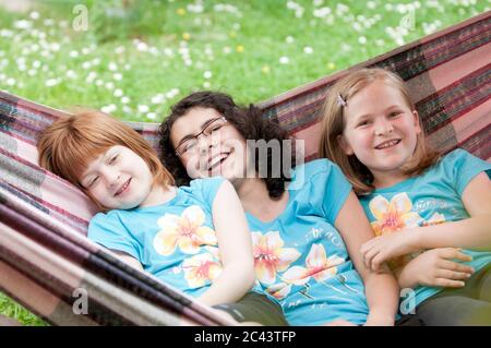 Three cheerful girls are lying in a hammock Stock Photo