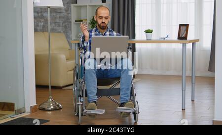 Businessman in wheelchair waving during a video call while working from home. Stock Photo