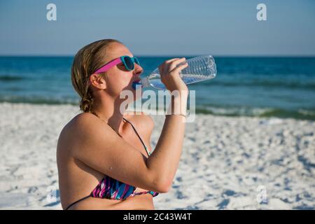 Young woman on the beach drinks from a water bottle, Destin, Florida, USA Stock Photo