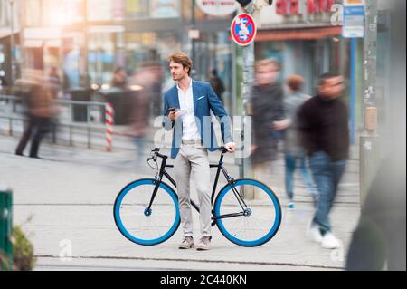 Portrait of young businessman with bicycle and smartphone waiting in the city Stock Photo