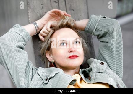 Close-up of thoughtful mature woman looking up while lying on concrete wall Stock Photo