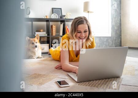 Happy woman with dog using laptop in living room at home Stock Photo