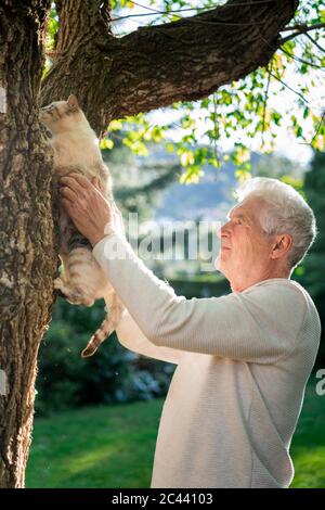 Senior with cat climbing on a tree in garden Stock Photo