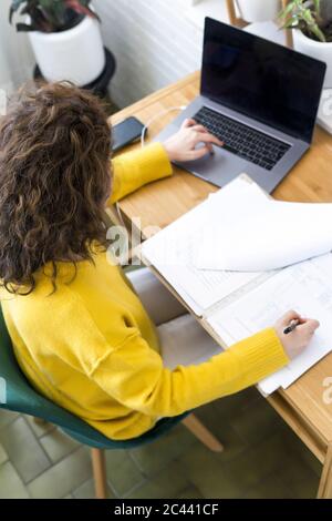 Woman working at desk in home office using laptop and taking notes Stock Photo