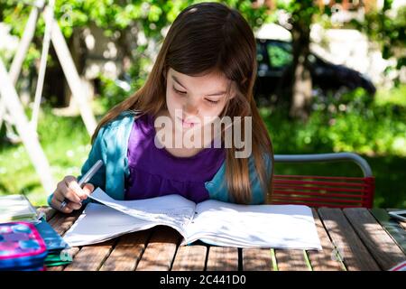 Girl sitting at garden table doing homework Stock Photo