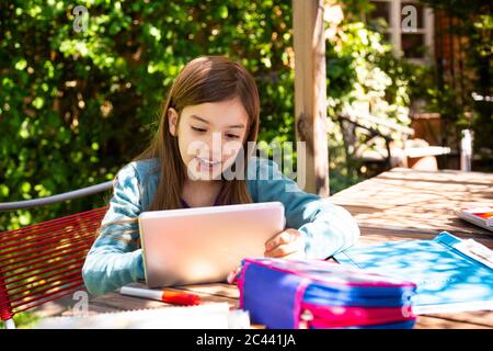 Girl sitting at garden table doing homework and using tablet Stock Photo