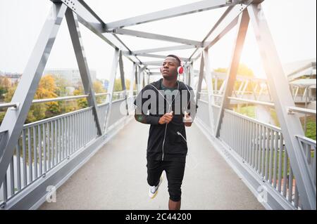 Young man with headphones jogging on footbridge Stock Photo