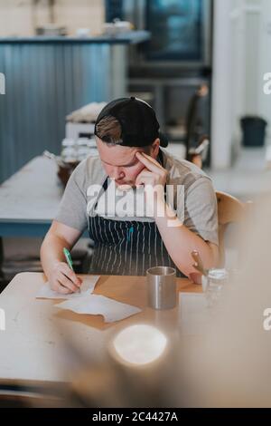 Worried young male owner sitting with receipts at table in restaurant Stock Photo