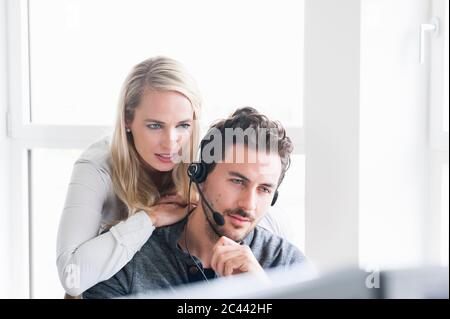 Businesswoman leaning on male customer service representative wearing headset while using computer in office Stock Photo