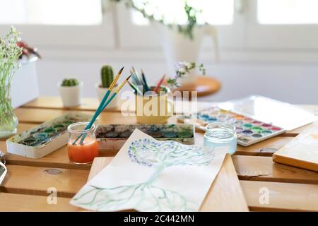 Watercolor paints with drawing and paintbrushes on wooden table home Stock Photo