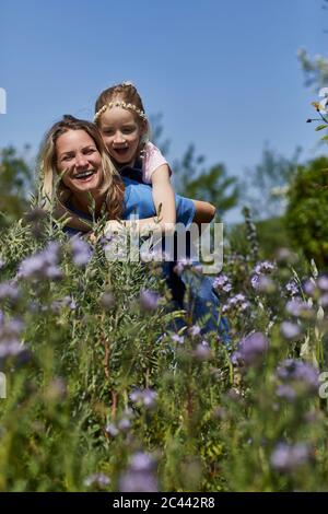 Happy mother carrying daughter piggyback in allotment garden Stock Photo