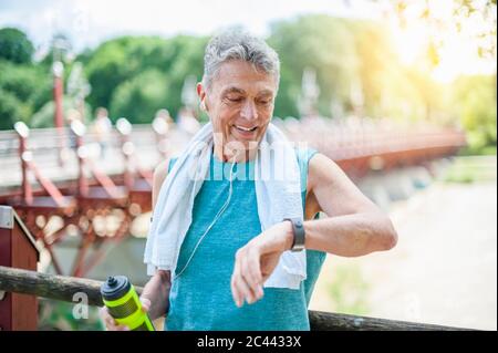 Smiling active senior man looking at smart watch while standing in park Stock Photo