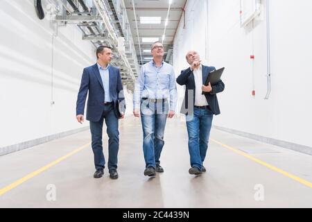 Three businessmen walking and talking on factory corridor Stock Photo