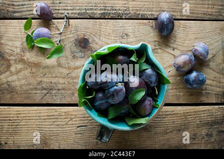 Jug of fresh plums standing on wooden surface Stock Photo