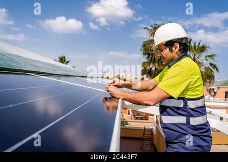 Mature technician installing solar panel on house roof against sky Stock Photo