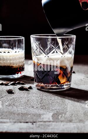 Cropped hand of woman pouring cream in White Russian cocktail on concrete table Stock Photo