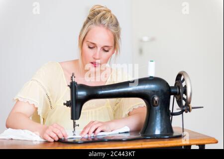 Portrait of blond young woman using old sewing machine Stock Photo