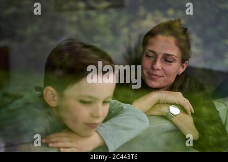 Thoughtful mother with son relaxing on sofa at home seen through window Stock Photo