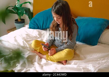 Girl using smartphone sitting on bed Stock Photo