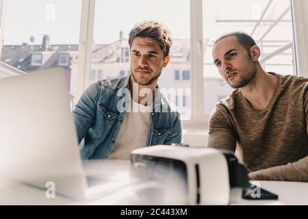 Two young busnessmen looking at laptop with VR goggles on desk Stock Photo