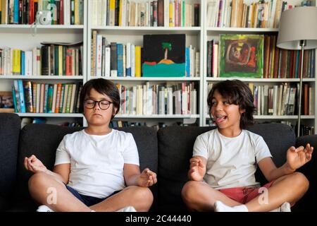 Boy sitting on couch meditating, his brother teasing him Stock Photo