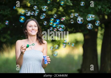 Happy young woman enjoying while looking at bubbles at park Stock Photo